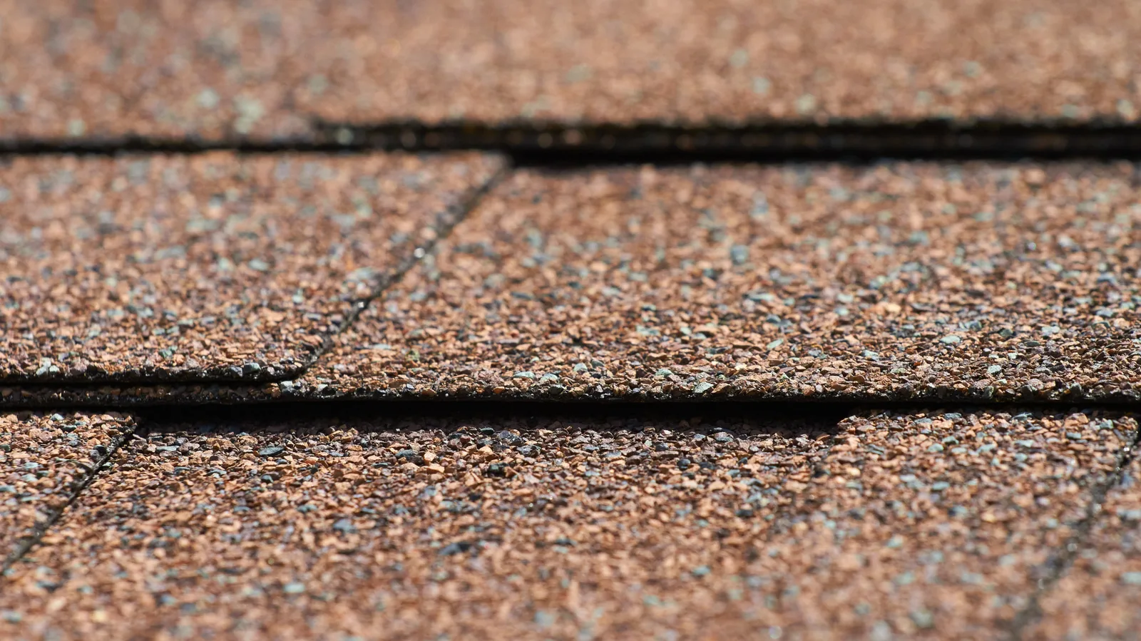 Macro of brown asphalt shingle granules and overlapping tab edges